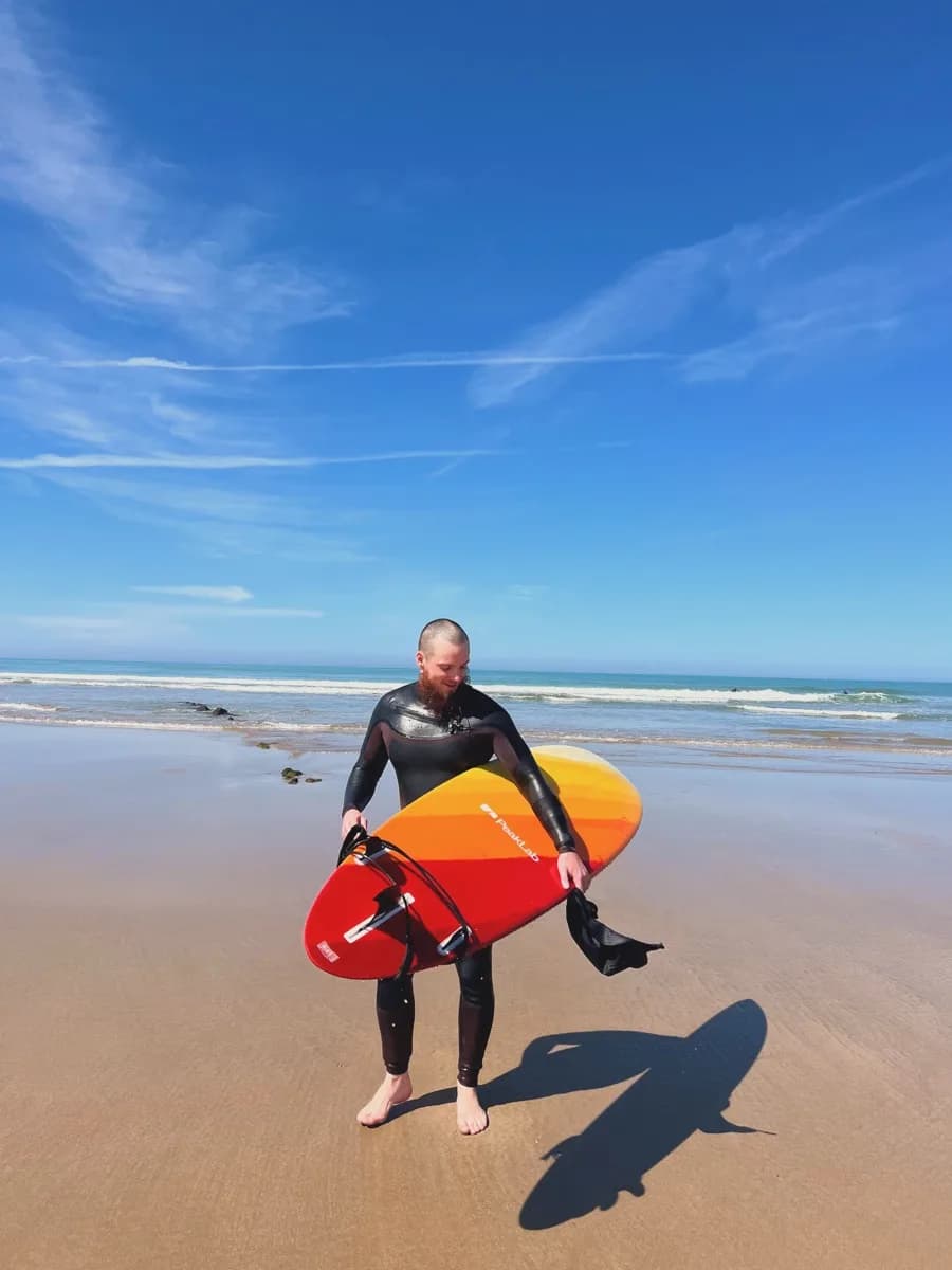 Lucien Arbieu sur la plage avec une planche de surf aux couleurs de PeakLab